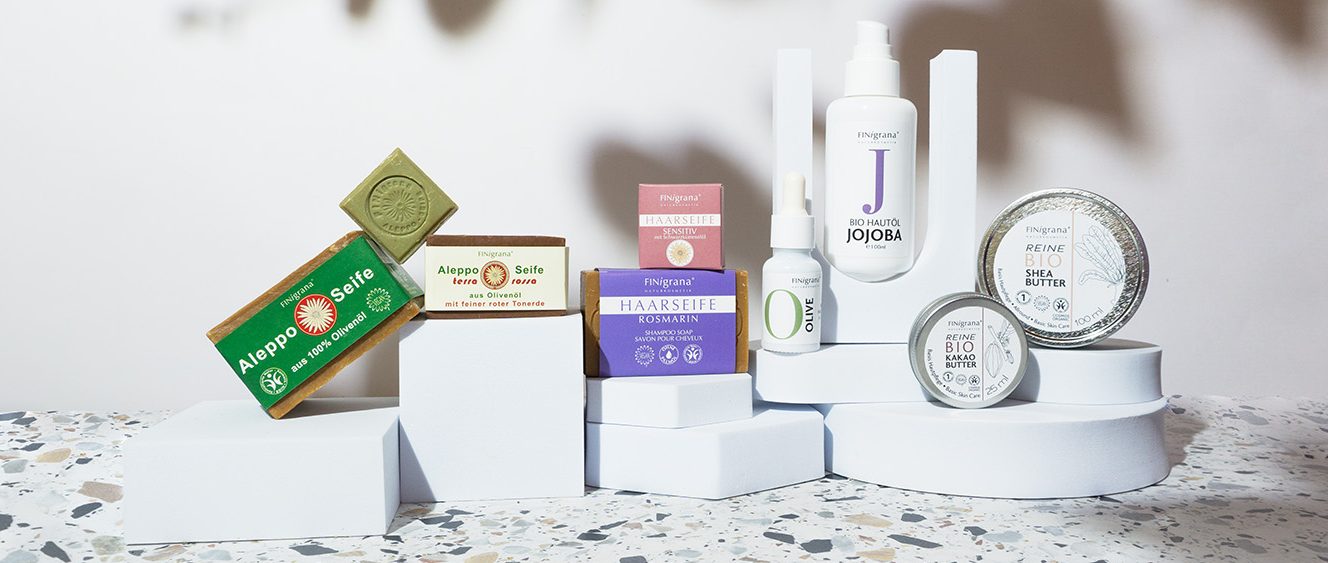 Finigrana Naturkosmetik Produktübersicht. Alepposeife gestapelt, Bio Buttter, Hautöle, Kokosöl im Glas und eine große Dose Reine Bio Sheabutter.