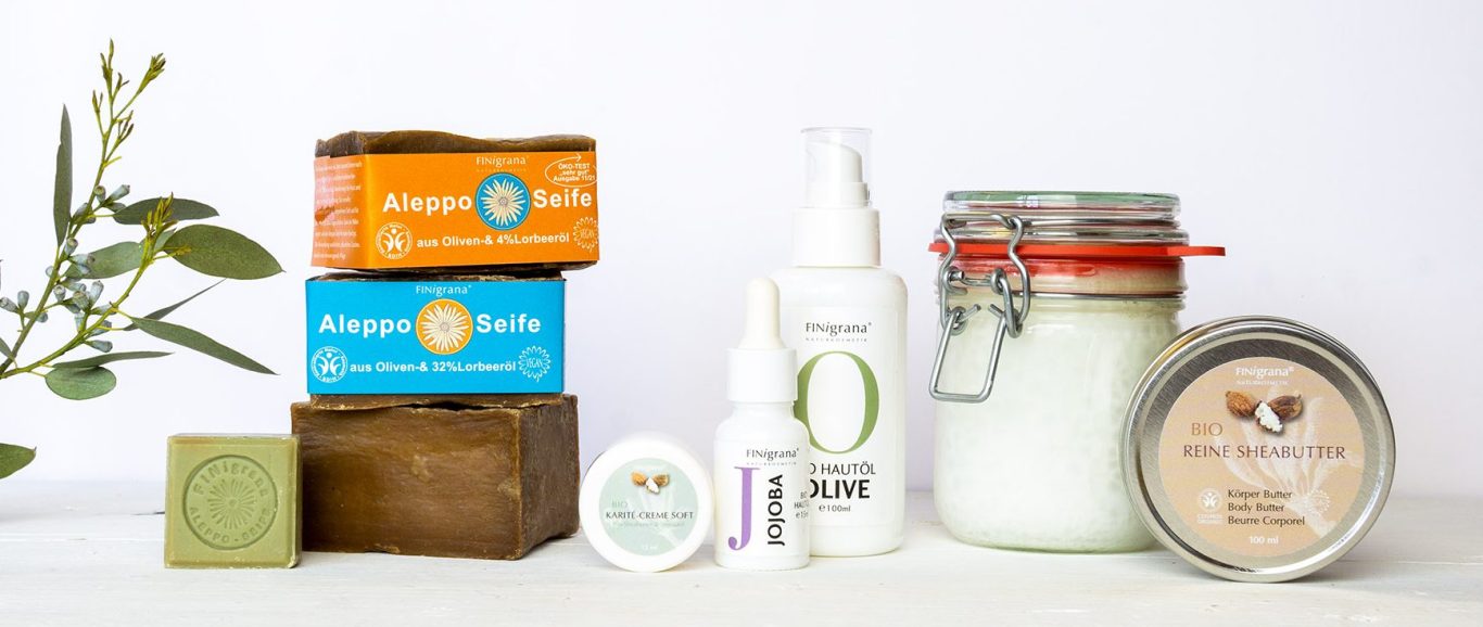 Finigrana Naturkosmetik Produktübersicht. Alepposeife gestapelt, Bio Buttter, Hautöle, Kokosöl im Glas und eine große Dose Reine Bio Sheabutter.