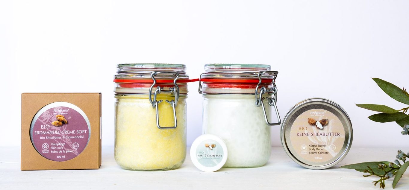 Übersichtsbild von unterschiedlichen Finigrana Bio Buttern. In der Mitte zwei in Gläsern mit Bügelverschluss, zwei links und rechts davon in Aludose. Eine davon on Pappumverpackung und in der Mitte eine kleine Butter in Kunststofftiegel.